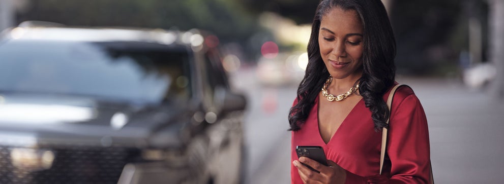 lady checking her mobile with a Cadillac vehicle background | Lindsay Cadillac of Alexandria in Alexandria VA